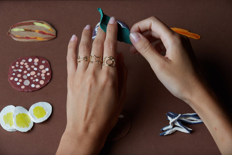 Hands wearing gold rings shaped like shark, cat, camera