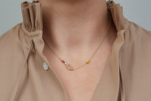 Gold chain necklace with gold tennis racquet and ball shaped pendants in pink and yellow enamel worn by model