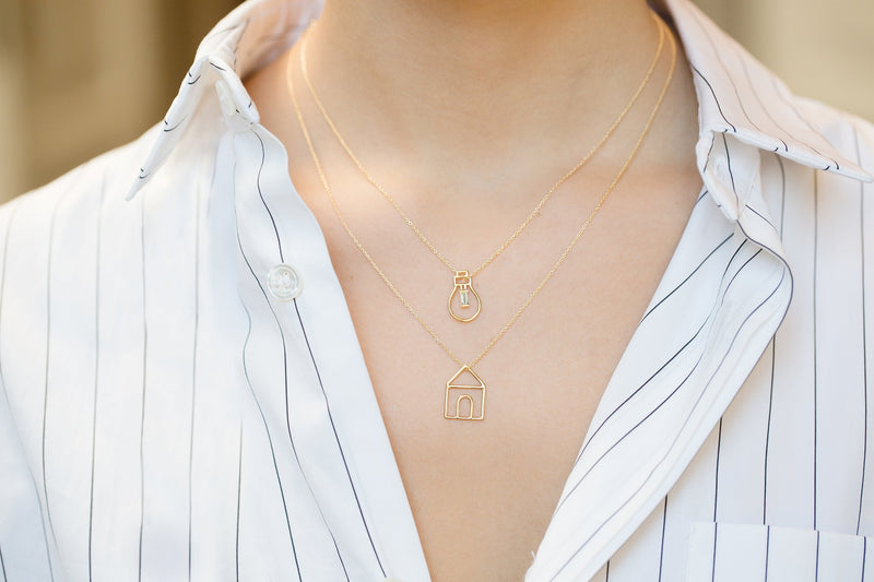 Gold chain necklaces with gold house and light bulb shaped pendants worn by model