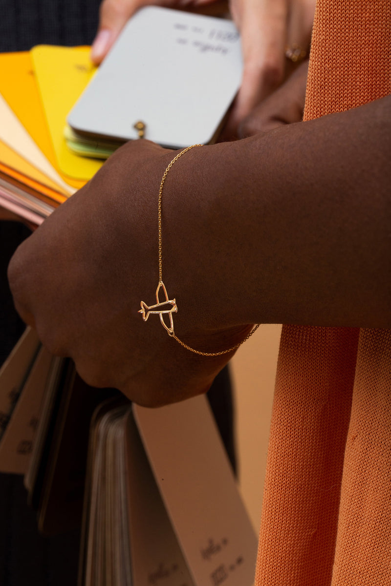 Gold chain bracelet with airplane shaped pendant on model's wrist