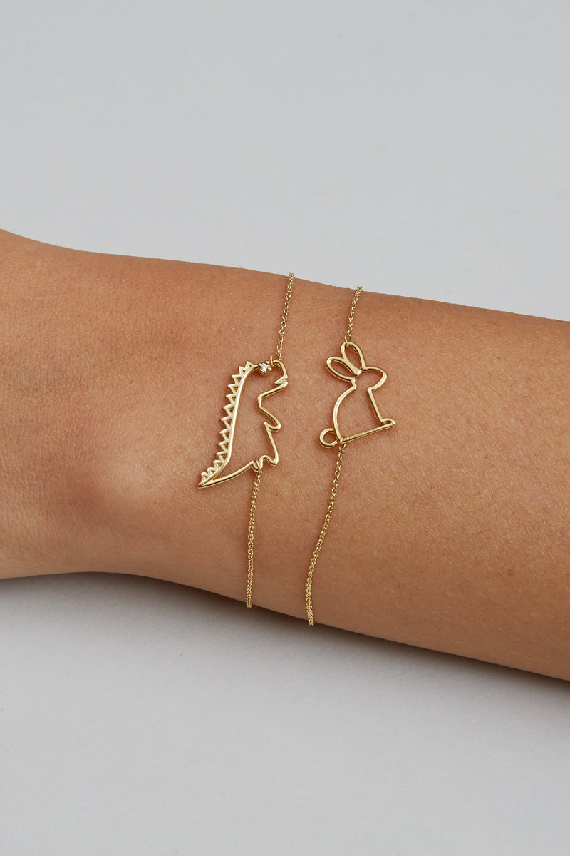 Gold chain bracelets with small rabbit and dinosaur shaped pendants on model's wrist