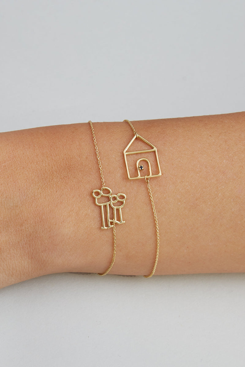 Gold chain bracelets with family and house shaped gold pendants on model's wrist
