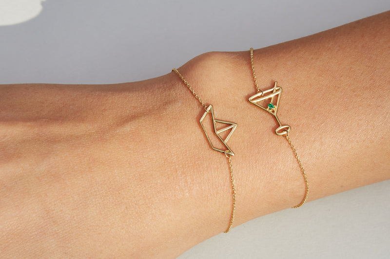 Gold chain bracelet with martini drink shaped pendant and small emerald worn by model