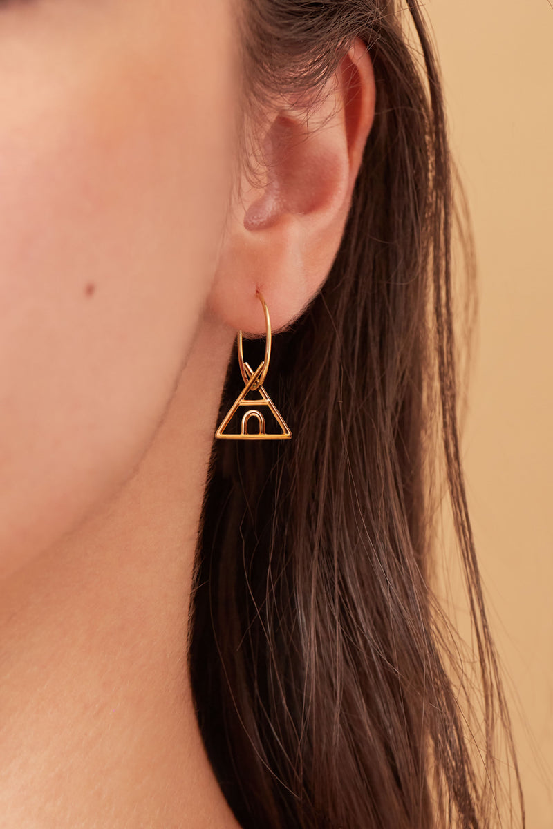 Gold hoop earring with indian tent shaped pendant worn by model
