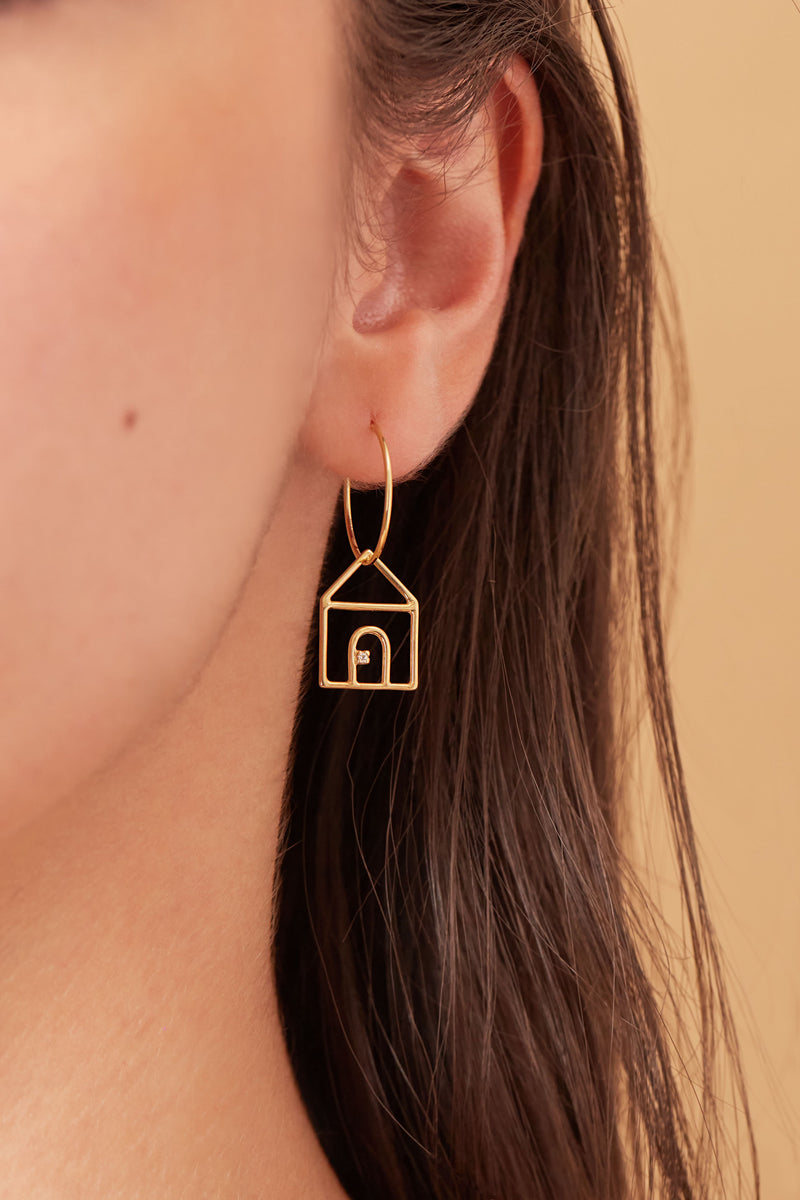 Gold hoop earring with house shaped pendant and small diamond worn by model