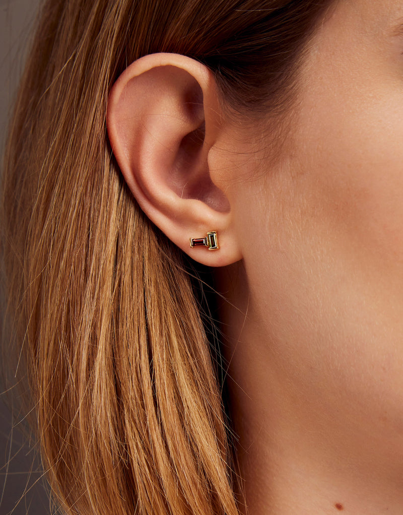 Gold earrings pair with baguette cut garnet and green tourmaline on woman
