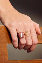 Load image into Gallery viewer, Hand wearing a rabbit shaped gold ring and a gold ring with porcelain cameo with an eggplant
