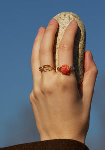 Hand wearing a crocodile shaped gold ring with diamond and a gold ring with a shell in red coral