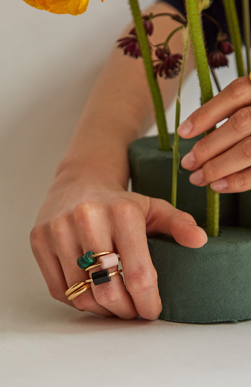 Hands wearing gold rings with cylinder cut malachite stones