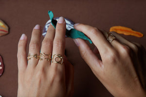 Hand wearing gold rings shaped like cat, camera, shark