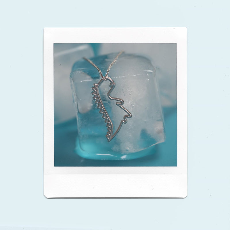White gold chain necklace with dinosaur shaped pendant on ice cubes