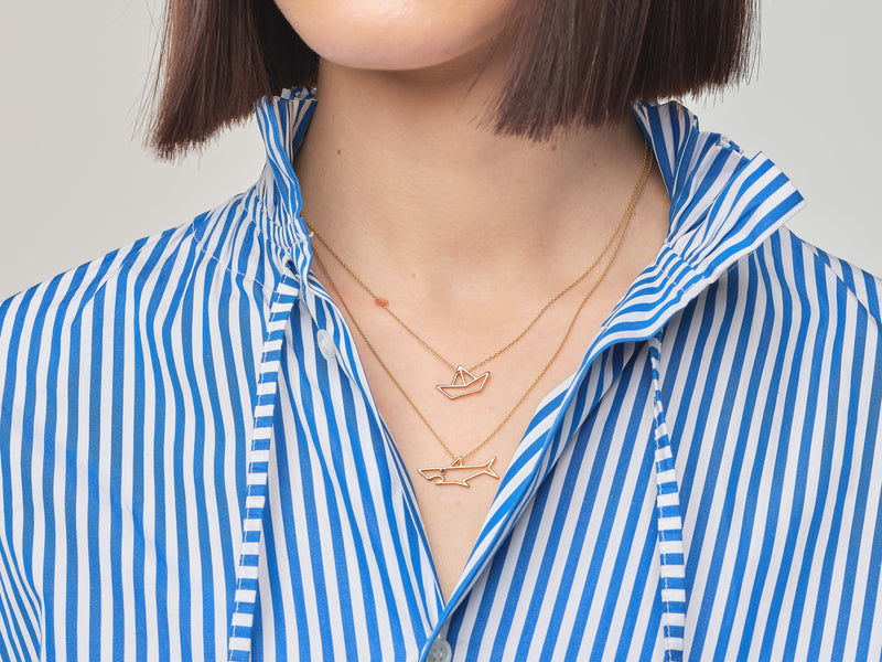 Model wearing gold chain necklaces with little boat and shark shaped pendantsGold chain necklace with shark shaped pendant with blue sapphire eye worn by model