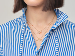 Model wearing gold chain necklaces with little boat and shark shaped pendants