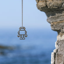 Load image into Gallery viewer, White gold chain necklace with robot shapde pendant and blue sapphires on a seaside background
