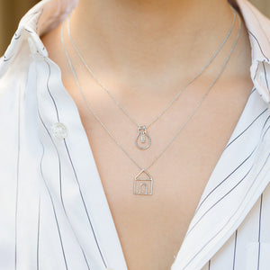 Model wearing white gold chain necklaces with house and light bulb chain pendants