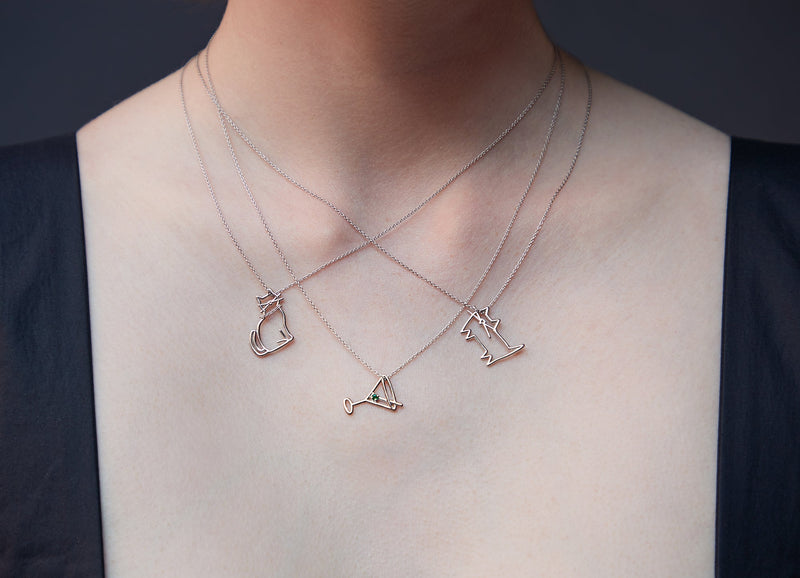 Woman wearing three white gold necklaces with a two cat shaped pendants and a martini cocktail shaped pendant
