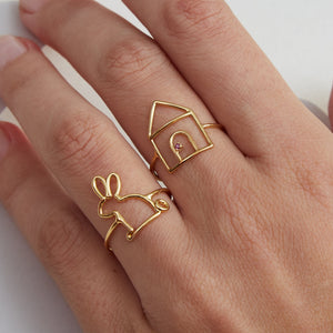 Woman wearing gold rings shaped like a little rabbit and a little house with ruby stone