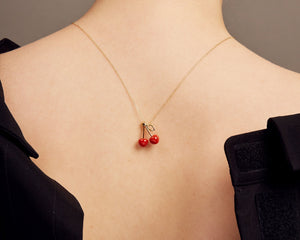 Woman shot from the back wearing a gold chain necklace with two cherries in red coral