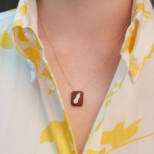 Woman wearing a gold chain necklace with an eggplant shaped cameo made in porcelain