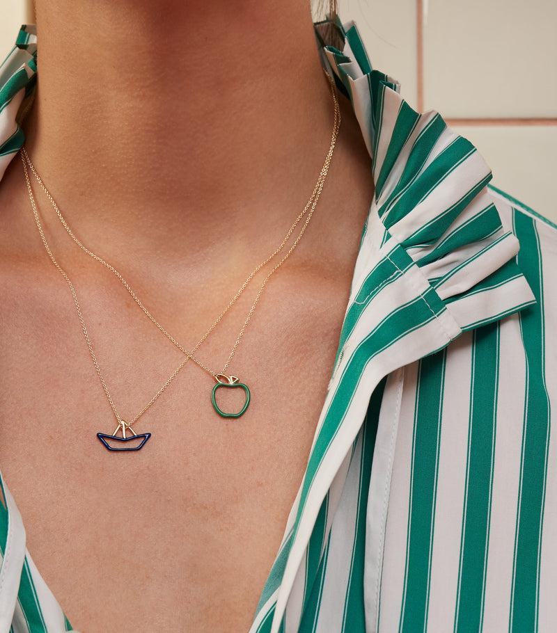 Woman wearing gold necklaces with a little boat pendant and a little apple pendant
