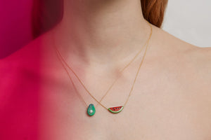 Woman wearing a gold chain necklace with a watermelon slice in red coral and a necklaces with avocado in green turquoise
