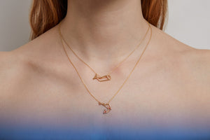 Woman wearing two gold necklaces with pendants shaped like a whale and a shrimp