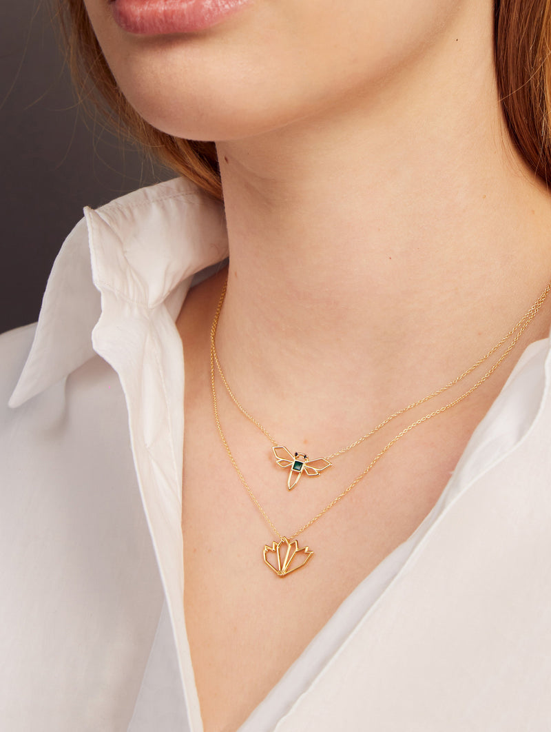 Woman wearing a gold necklace with a dragonfly shaped pendant and a gold necklace with a waterlily shaped pendant